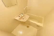 寮のユニットバス。浴槽、洗面台、シャワーが一体化された、クリーム色のコンパクトな浴室。