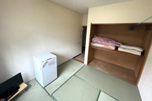 リゾートバイトの個室寮の室内。畳敷きの部屋にミニ冷蔵庫とテレビが備え付けられ、クローゼットも見える、シンプルな寮の部屋の画像。