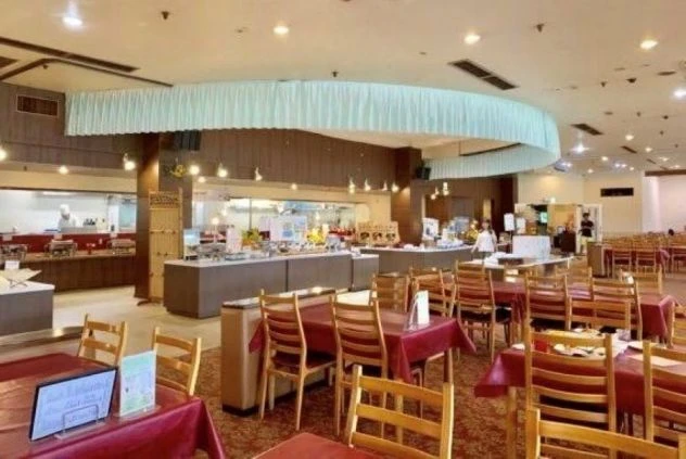 ホテルのビュッフェレストランのダイニングの画像。たくさんのテーブルとビュッフェカウンターが並び、シェフが料理を提供している様子が見える。