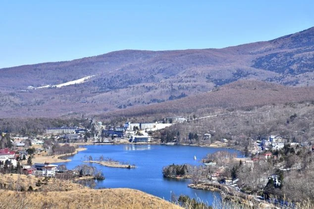 山々に囲まれた湖の風景の画像。青い湖面と、その周りに広がる建物や木々が美しい景観を作り出している。リゾートバイトの休日の過ごし方や観光を表す画像
