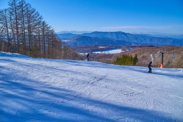 スキー場のゲレンデから、遠くに広がる雪山と街並みを見下ろす雄大な風景の画像。青空の下でスキーヤーが滑走している。リゾートバイトの休日の過ごし方や冬の景色を表す画像。