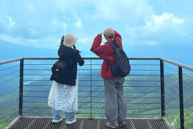 山々を背景にした展望台で、若い女性2人が遠くの景色を指さしている後ろ姿の画像。リゾートバイトの休日の過ごし方や観光を表すワクトリオリジナル画像。