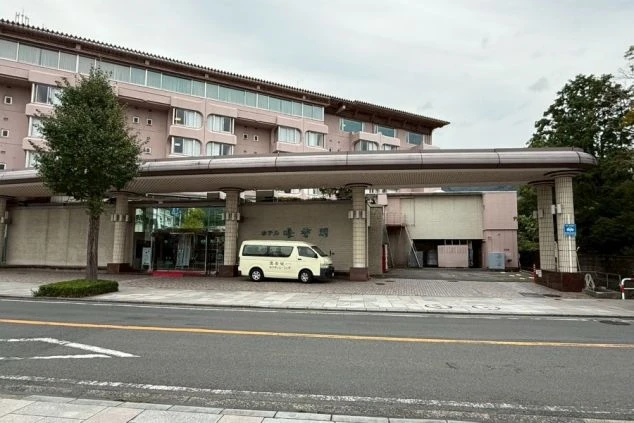 ピンクベージュの外壁の大きな建物で、庇の下にエントランス