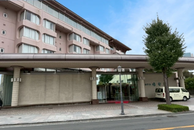 ピンクベージュの外壁の大きな建物で、庇の下にエントランス