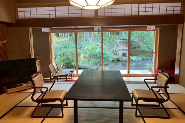 伝統的な日本の旅館の玄関。瓦屋根のついた重厚な門構えで、木製の縦格子戸が開いている。