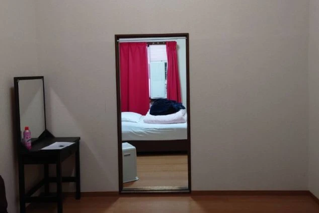 リゾートバイトの寮の部屋。ドレッサーと鏡があり、奥の部屋と繋がっている。快適な生活を送れる寮設備。