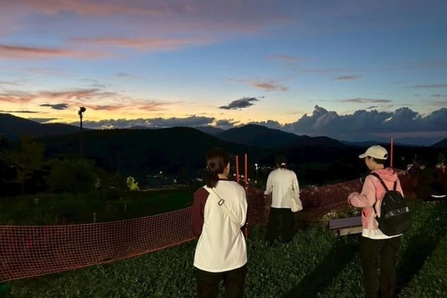 夜明け前の山々を背景に、若い男女3人が景色を眺めている後ろ姿の画像。空がオレンジ色や青色に染まり、幻想的な雰囲気を醸し出している。リゾートバイトの休日の過ごし方やリゾート地の風景を表す画像。