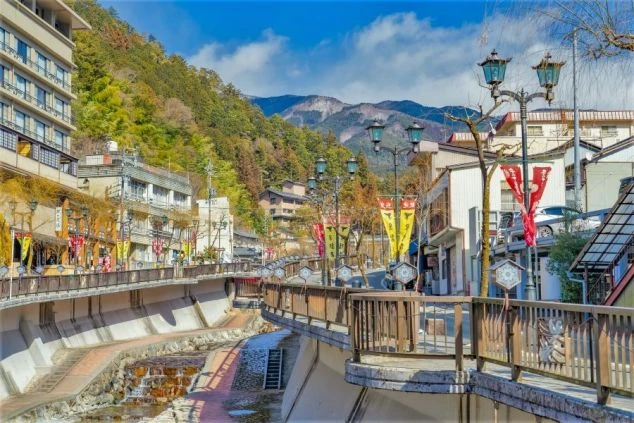 山に囲まれた温泉街の川沿いの遊歩道と街並みの風景。リゾートバイトを通して、このような風情ある観光地を散策し、旅気分を味わえる魅力を伝えます。