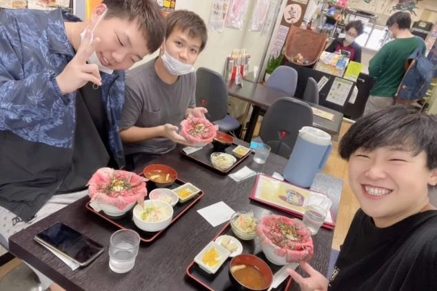 ボリューム満点のローストビーフ丼を囲み、笑顔でポーズをとるリゾートバイトの仲間たちの写真。仲間とご当地グルメを楽しめる魅力を伝えます。