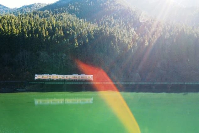 エメラルドグリーンの湖を渡る列車の絶景写真。リゾートバイトの勤務地へ向かう旅の始まりや、非日常的な鉄道の旅を楽しめる魅力を表現しています。