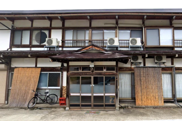 趣のある古い木造建築を利用した、どこか懐かしい雰囲気の民宿タイプのスタッフ寮外観の画像。