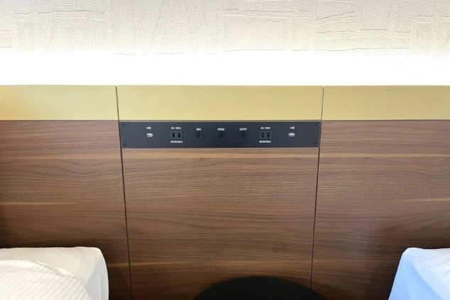 ベッドのヘッドボードに設置されたコントロールパネル。ACコンセント2口、USBポート2口、照明スイッチが並び、手軽に充電や調光ができる便利な枕元の設備。