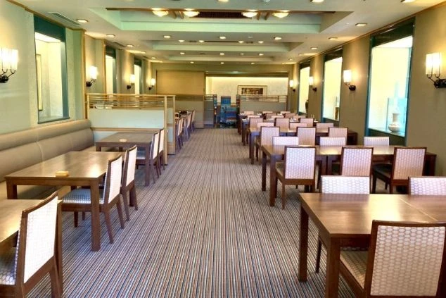 木製テーブルと椅子が整然と並ぶ、ホテルの広々としたダイニングルームの写真。リゾートバイトの仕事を通して、このような落ち着いた空間で、丁寧な接客やサービスを学べる魅力を伝えます。