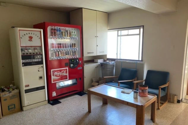リゾートバイト寮の共用スペース。飲料とタバコの自動販売機が置かれ、テーブルと椅子もあり、仕事の合間に休憩できる設備の画像。