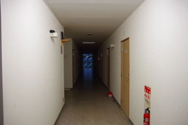 リゾートバイト寮の廊下。各個室のドアが並び、奥には共用スペースが見える、住み込み生活の雰囲気が伝わる寮の画像。