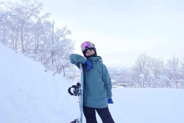 雪化粧の木々が美しいスキー場でスノーボードを持つ女性。冬のリゾートバイトの仕事の合間や休日に雪山を楽しむ。