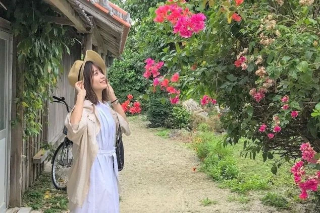 南国の花が咲くのどかな道を散策する女性の写真。リゾートバイトを通して、非日常的な南国リゾートで癒しの時間を過ごせる魅力を伝えます。