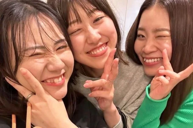 笑顔でポーズをとるリゾートバイトの仲間3人組の自撮り写真。寮生活を通して出会い、友情を深める若者の楽しい日常を表現しています。