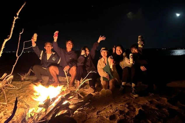 夜のビーチで焚き火を囲み、乾杯するリゾートバイトの仲間6人の写真。寮生活を通して出会った友人たちと、非日常的な最高の思い出を作れる魅力を伝えます。