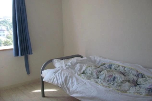 リゾートバイトの寮の部屋の画像。シンプルなシングルベッドと窓に水色のカーテンがかかっており、プライベート空間が確保されている。