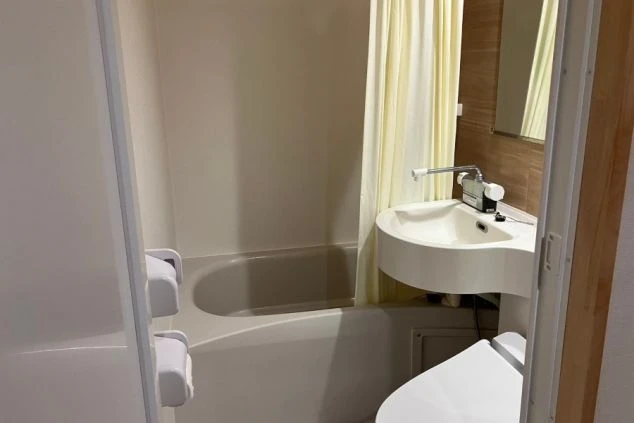 寮のユニットバス。浴槽とシャワー、トイレ、洗面台、鏡が映る。