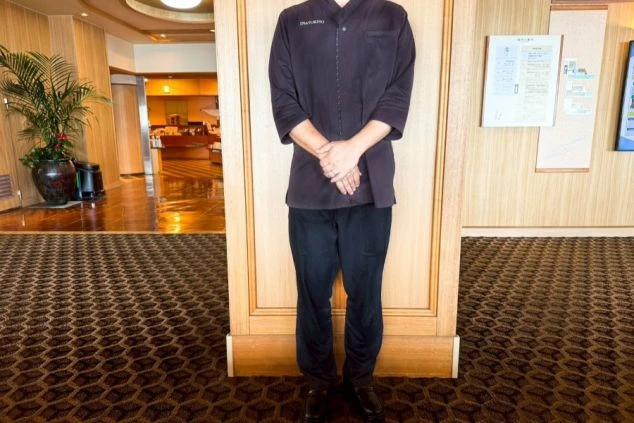 接客係の夏服を着た男性。濃い色の作務衣のような上着に、黒いパンツを着用している。