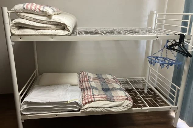 リゾートバイトの寮にある二段ベッド。清潔な寝具が用意されており、個室または相部屋での生活を想像させる画像。