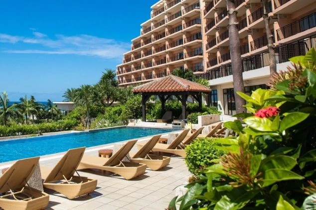 澄み切った青空の下、南国の雰囲気が漂うホテルのプールと外観。