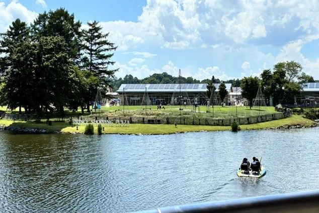 軽井沢・プリンスショッピングプラザのアウトレットモールの外観を湖越しに見た画像。湖面には水上ボートに乗った人が見え、広々とした芝生が広がっている。リゾートバイトの休日の過ごし方や周辺環境を表す画像。