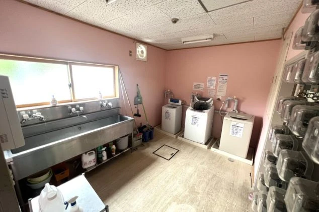 リゾートバイト寮の共用ランドリースペース。複数の洗濯機と大きなシンクが設置されており、長期滞在でも不便なく利用できる設備の寮画像。