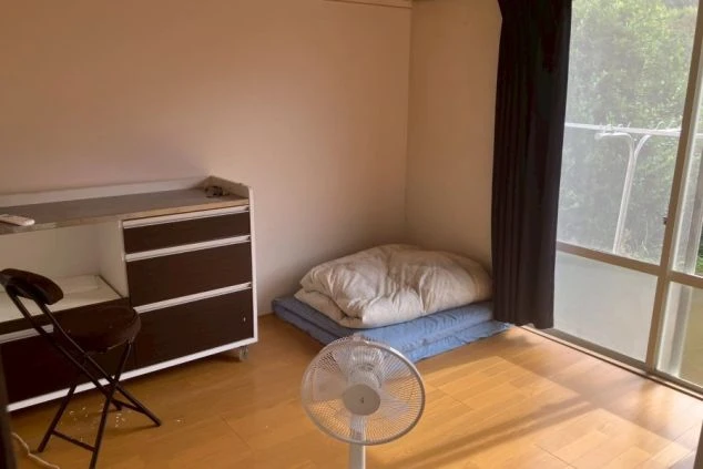 リゾートバイトの寮の寝室。フローリングの床に布団が敷かれており、デスクと大きな窓がある明るい洋室。