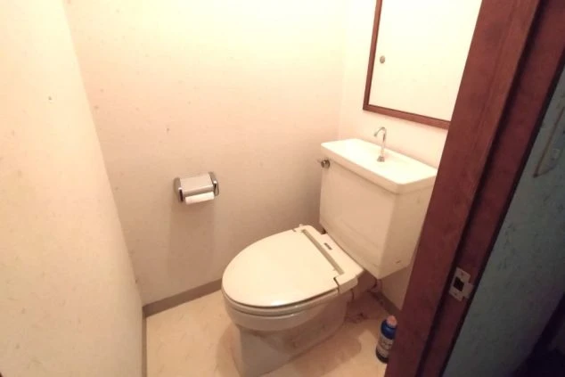 寮のトイレ。洗面台付きのトイレ、鏡、トイレットペーパーホルダーが映る。