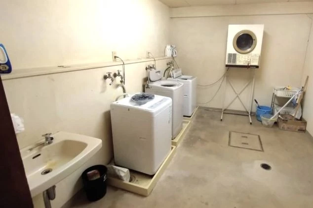 寮のランドリー。洗濯機、乾燥機、シンクが並ぶ共用スペースが映る。