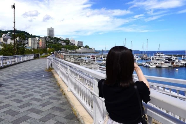静岡県熱海の親水公園から港のヨットハーバーを撮影する女性。リゾートバイトの休日に散策できる海辺の観光スポット。