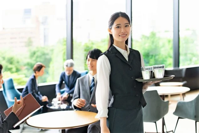 ホテルやレストランで働く女性スタッフ。トレイに水を乗せて運ぶホールスタッフの仕事風景。接客やサービス業のリゾートバイト。