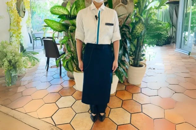 白い長袖シャツと紺色のロングエプロンを着用した、レストランスタッフの制服。リゾートバイトでレストランのホール業務を検討している方に、働く際の服装が伝わる画像。