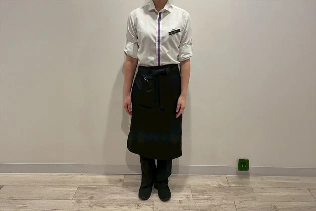 白い長袖シャツと黒いロングエプロンを着用したベルスタッフの制服。