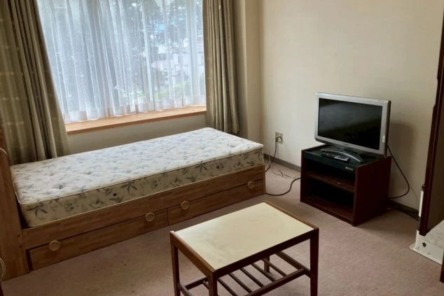 リゾートバイトの個室寮の室内の画像。ベッド、テレビ、テーブルが備え付けられており、家具家電付きの寮を探す人向け。