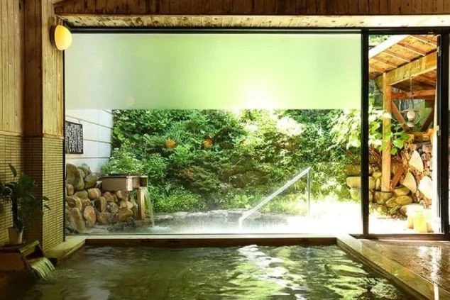 窓外の緑豊かな景色を眺めながら入浴できる、開放的なホテルの大浴場の画像。