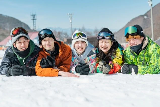 スキーウェアを着用した若い男女5人が、雪の上に腹ばいになって笑顔でカメラにポーズをとっている画像。冬のリゾートバイトを通じてできた仲間たちの楽しそうな雰囲気が伝わる画像。