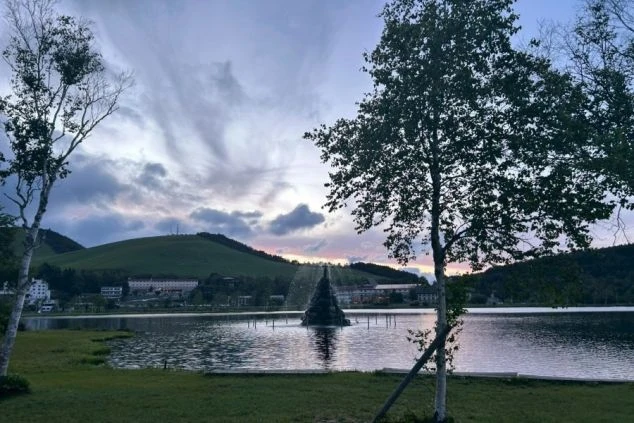 夕暮れの白樺湖の風景の画像。湖の中央に噴水のようなイルミネーションが見え、周囲には山や木々、ホテルが写っている。リゾートバイトの休日の過ごし方や観光を表す画像。