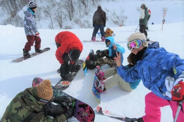 スキー場の雪原で、スノーボードやスキーを楽しむ若者たちのグループが休憩している画像。冬のアクティビティを楽しむリゾートバイト仲間の楽しそうな雰囲気が伝わるワクトリスタッフが撮影したオリジナル画像。