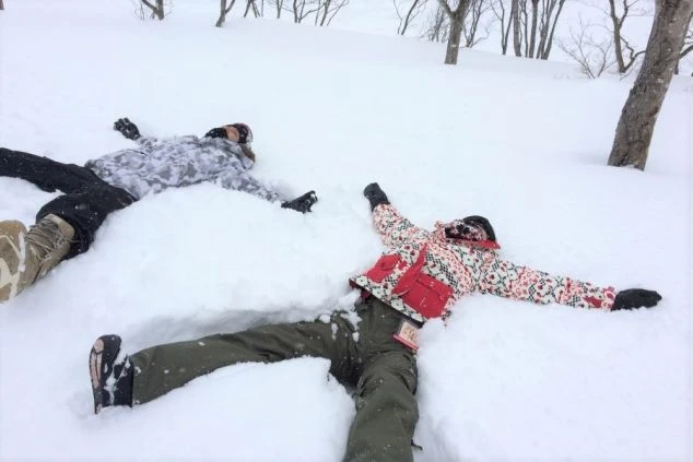 スキーウェアを着用した若い男女2人が、雪の上に大の字になって寝転び、雪遊びを楽しんでいる画像。リゾートバイトの休日の過ごし方や冬のアクティビティを表すワクトリスタッフが撮影したオリジナル画像。