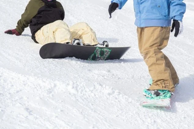 雪山のゲレンデで、スノーボードウェアを着用した2人のスノーボーダーが雪の上で休憩しているクローズアップ画像。リゾートバイトの休日の過ごし方や冬のアクティビティを表す画像。