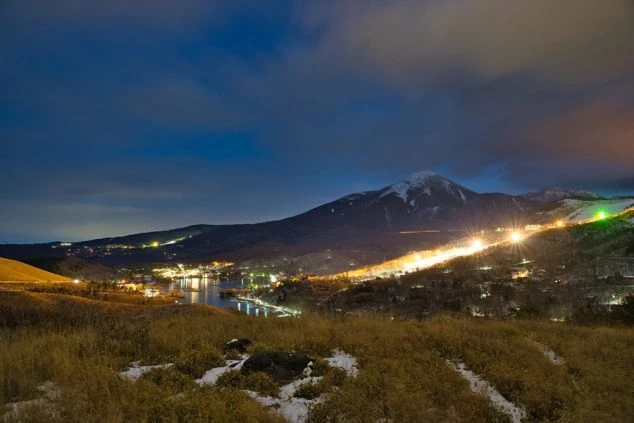 雪化粧をした山々と夜景が広がる雄大な風景の画像。湖畔の街がライトアップされ、リゾート地の幻想的な夜景が楽しめる。リゾートバイトの休日の過ごし方やリゾート地の風景を表す画像。