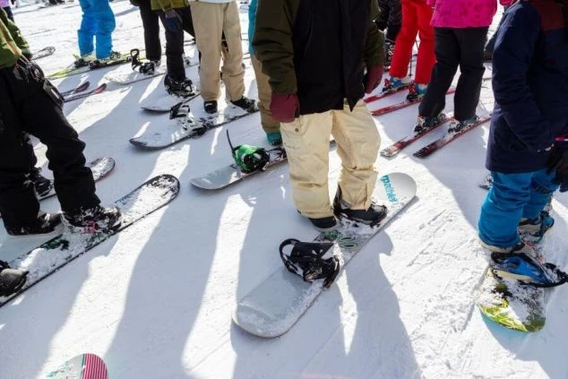 スキー場の雪の上に立つスノーボードを楽しむ人々の足元の画像。カラフルなボードやウェアが写り、冬のアクティビティの活気ある雰囲気が伝わる。リゾートバイトの休日の過ごし方や冬のアクティビティを表す。