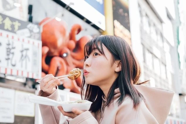 大阪・道頓堀の街中で、たこ焼きを美味しそうに頬張る女性。リゾートバイトの休日に、本場の味を楽しむのも醍醐味です。