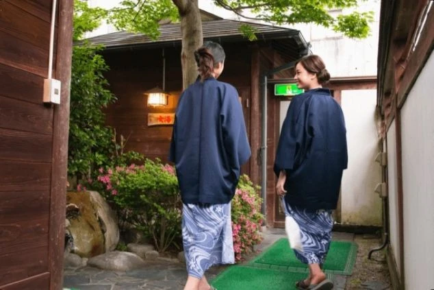 温泉旅館の中庭のような通路を浴衣姿の女性2人が歩いている。