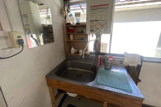 リゾートバイト寮の2階の共用廊下の画像。木目調の扉と白い壁が続き、階段や窓が写っている。リゾートバイトの寮の共用スペースの画像。