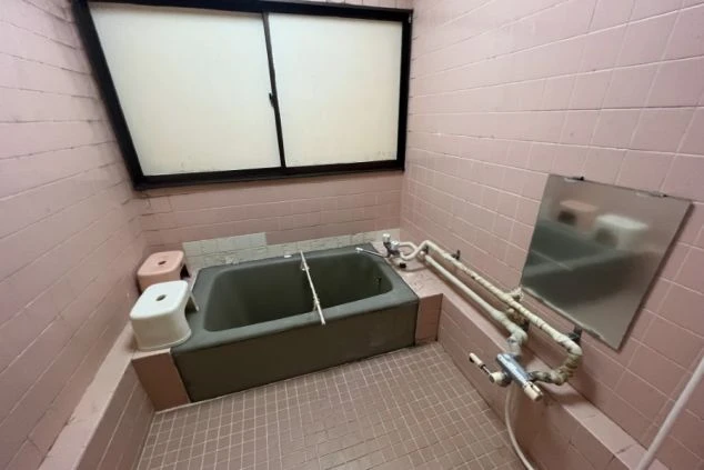 リゾートバイト寮の共同風呂の画像。ピンク色のタイルが特徴的で、浴槽とシャワーが備え付けられている。リゾートバイトの寮の風呂場の画像。